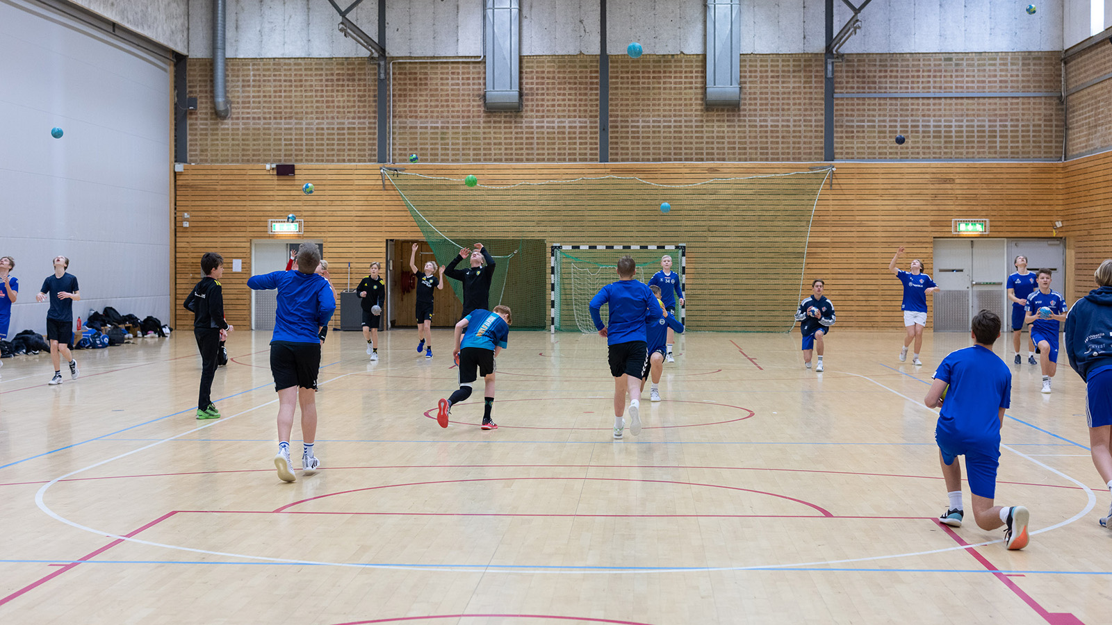 ett foto. spelare klädda i blått syns med ryggarna springandes i en handbollshall